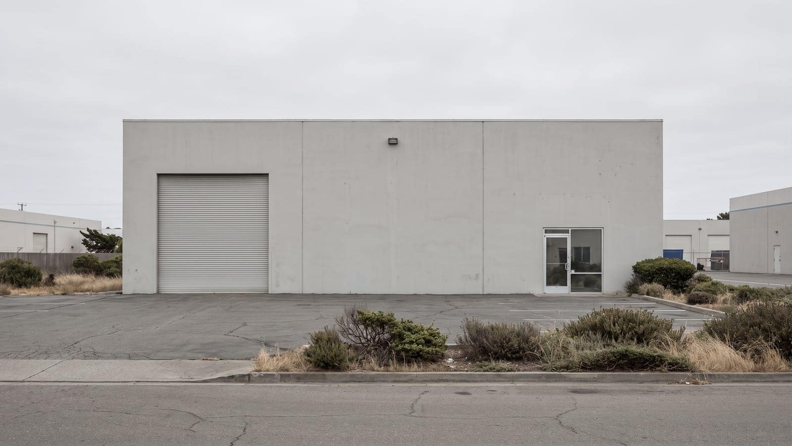 Single-unit industrial warehouse with concrete walls and a roll-up loading door in a light-industrial park.